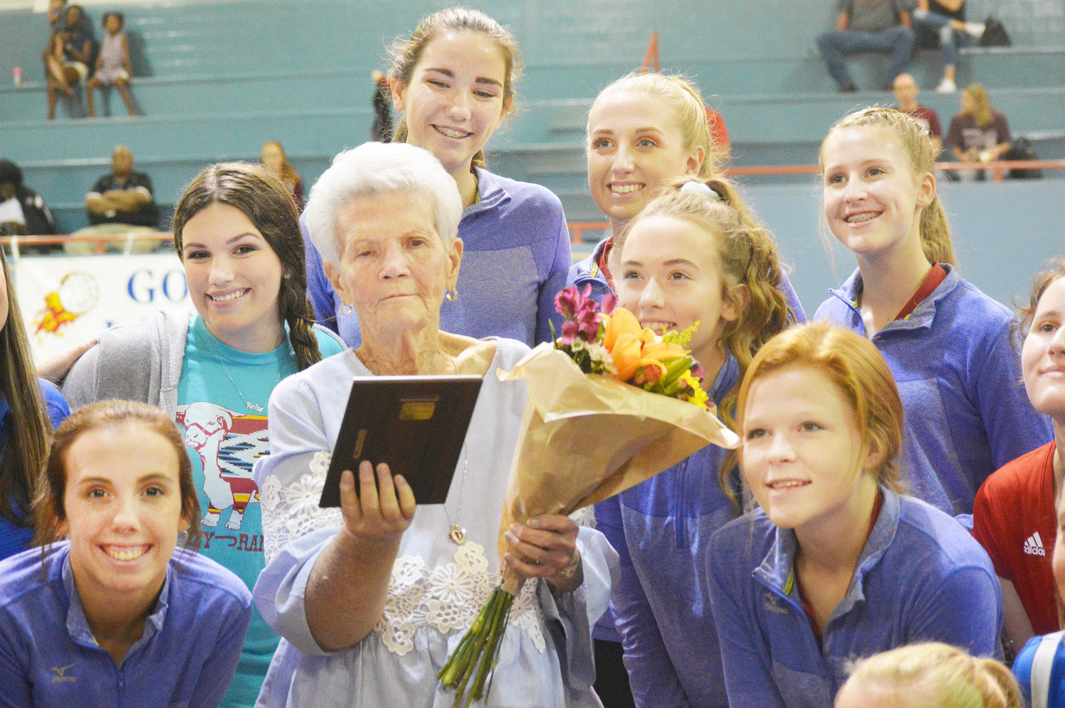 Former Quitman High School educator and coach Pat Neighbors is surrounded by the current Lady Bulldog volleyball team as she receives a plaque and flowers when being honored prior to the game last Tuesday at Ballard Memorial Gym.