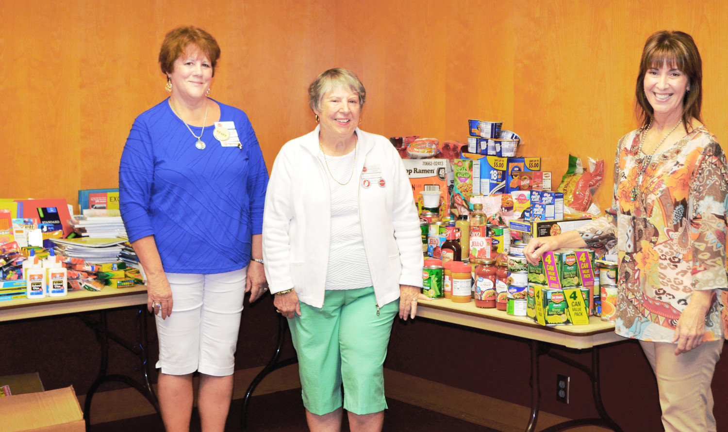 A total of 346 pounds of food were donated last week to the Kindness Cottage Food Bank by RV enthusiasts who attended the SMART National Muster last week at the Mineola Civic Center. The table to the left is heaped with school supplies also donated by SMART. They will benefit schools in Mineola. From left are SMART members Gwen Hopper of Nevada and Sally Kavanaugh of Arizona and BJ Gold, director of the Kindness Cottage.