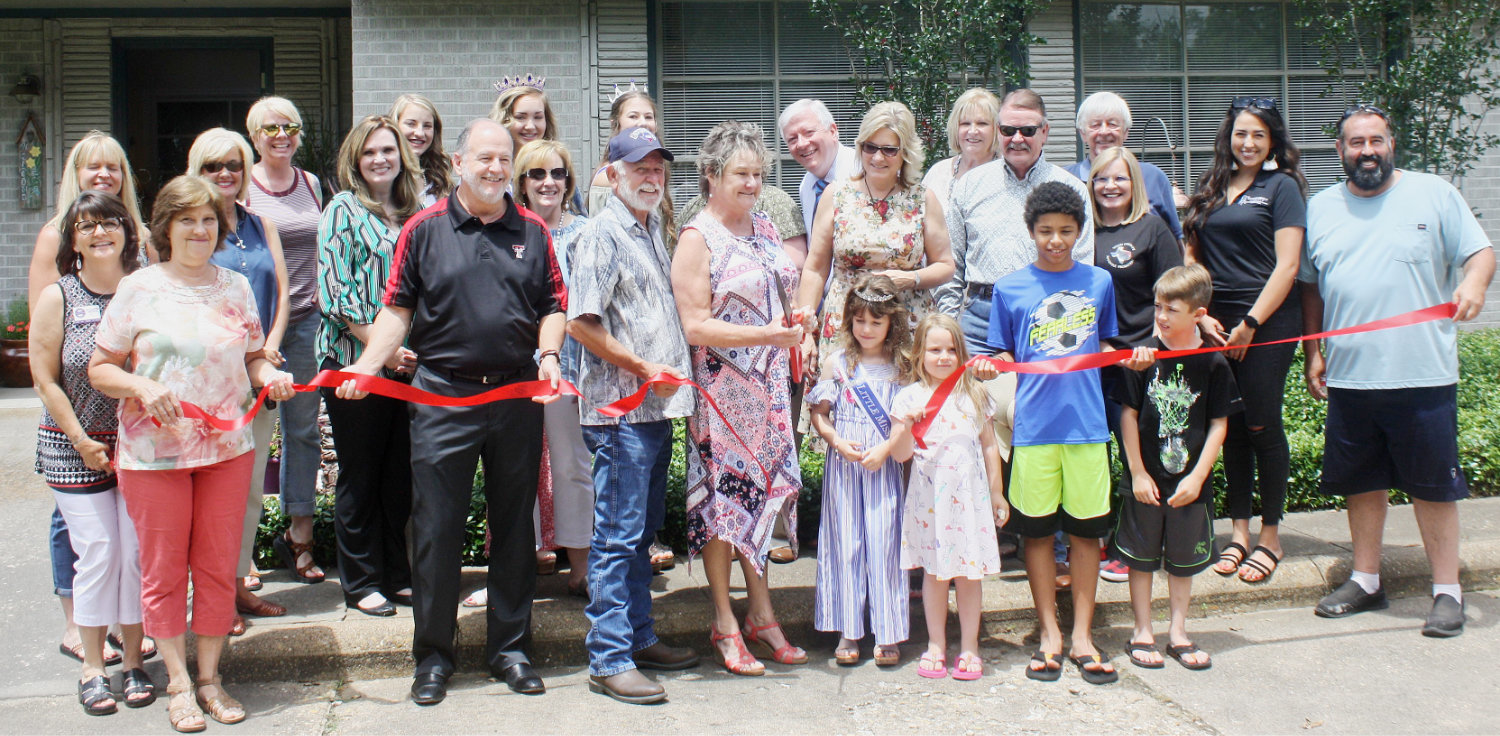 Julie Watson, co-owner of JK Business Services, cuts the ceremonial ribbon to signify the grand opening of the new business alongside community members, Dogwood queens and Quitman Chamber of Commerce directors.