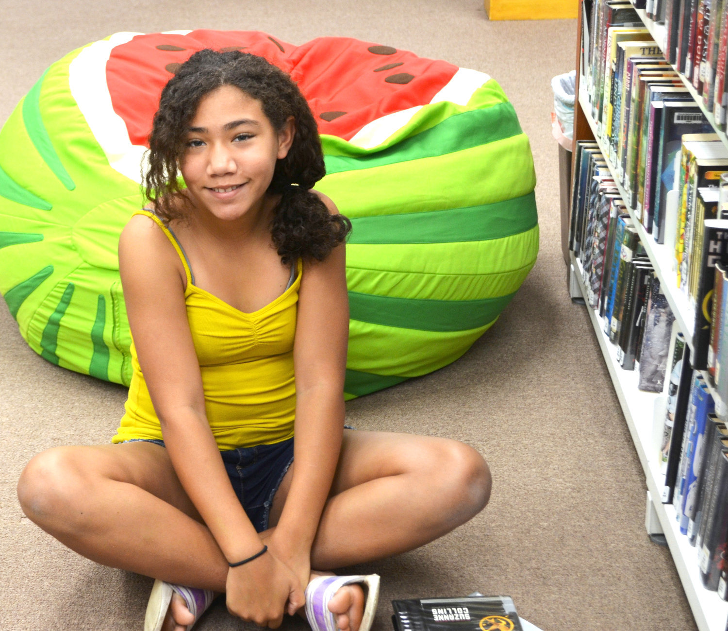 Allie Neagle of Mineola relaxes at the library’s area for teenage readers. The watermelon beanbag chair behind her is one of the many new additions to the library. (Monitor photo by Hank Murphy)