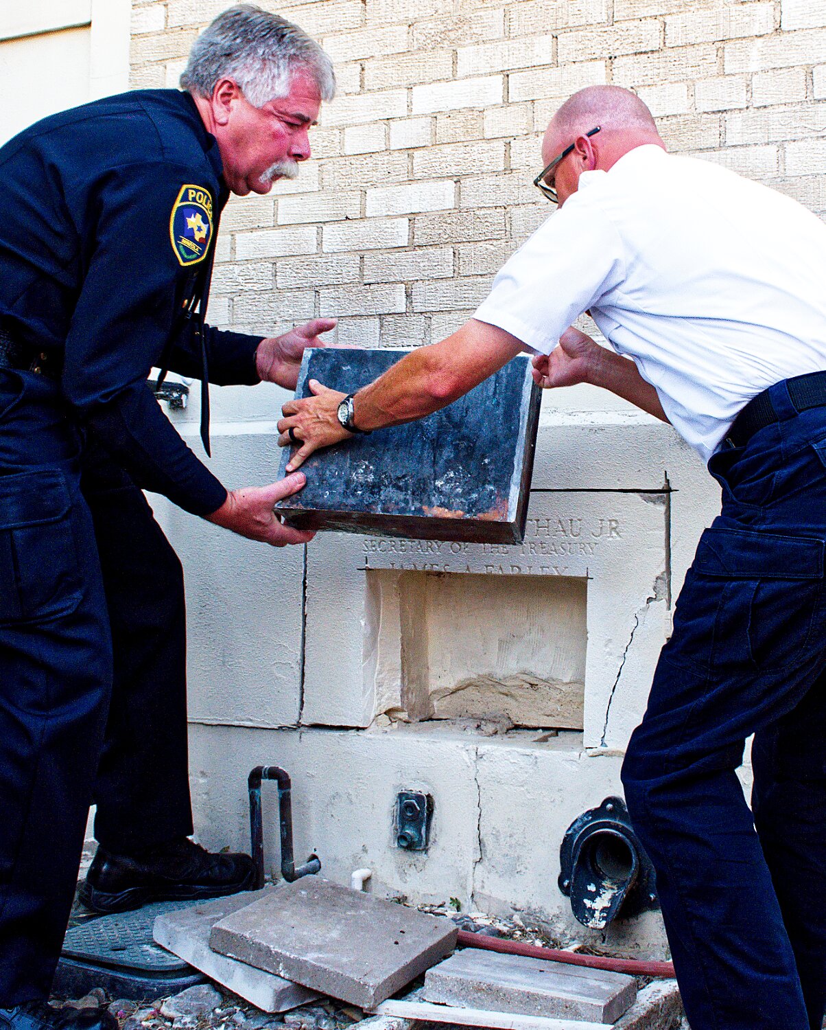 Police Chief Chuck Bittner and Fire Marshal David Madsen remove the metal box from the cornerstone for the former Mineola post office Saturday morning.