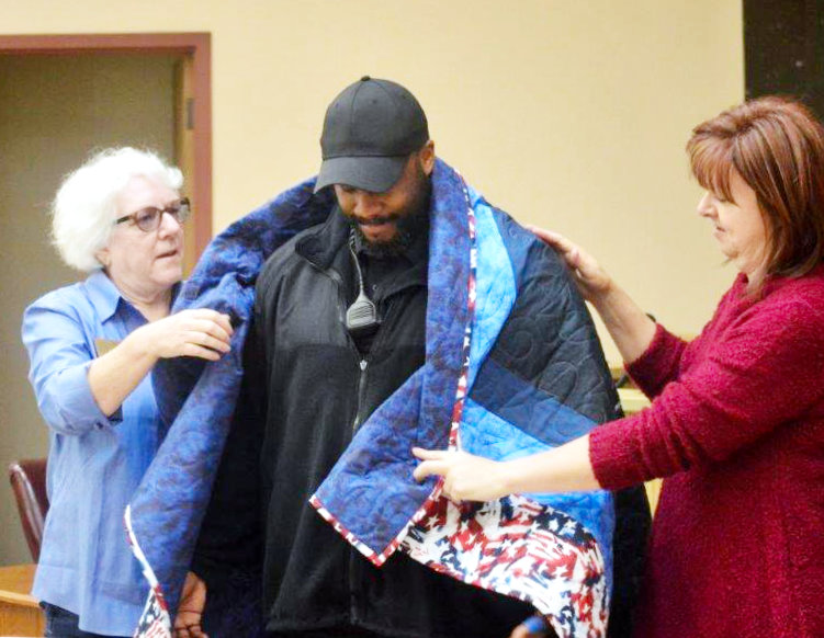 Quitman’s Chris Davis is shown being “wrapped” by two volunteers at the second annual Quilts of Valor awards ceremony in the courtroom at the Wood County Law Enforcement facilities on Stephens St.