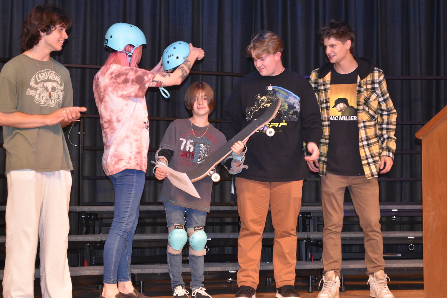 Brayden Williams (center) receives his Mineola Skate Club helmet and skateboard at last week’s graduation from coaches, from left, Preston Radla, Catherine Spurgeon, Brian Bethel and Nathan Witt.