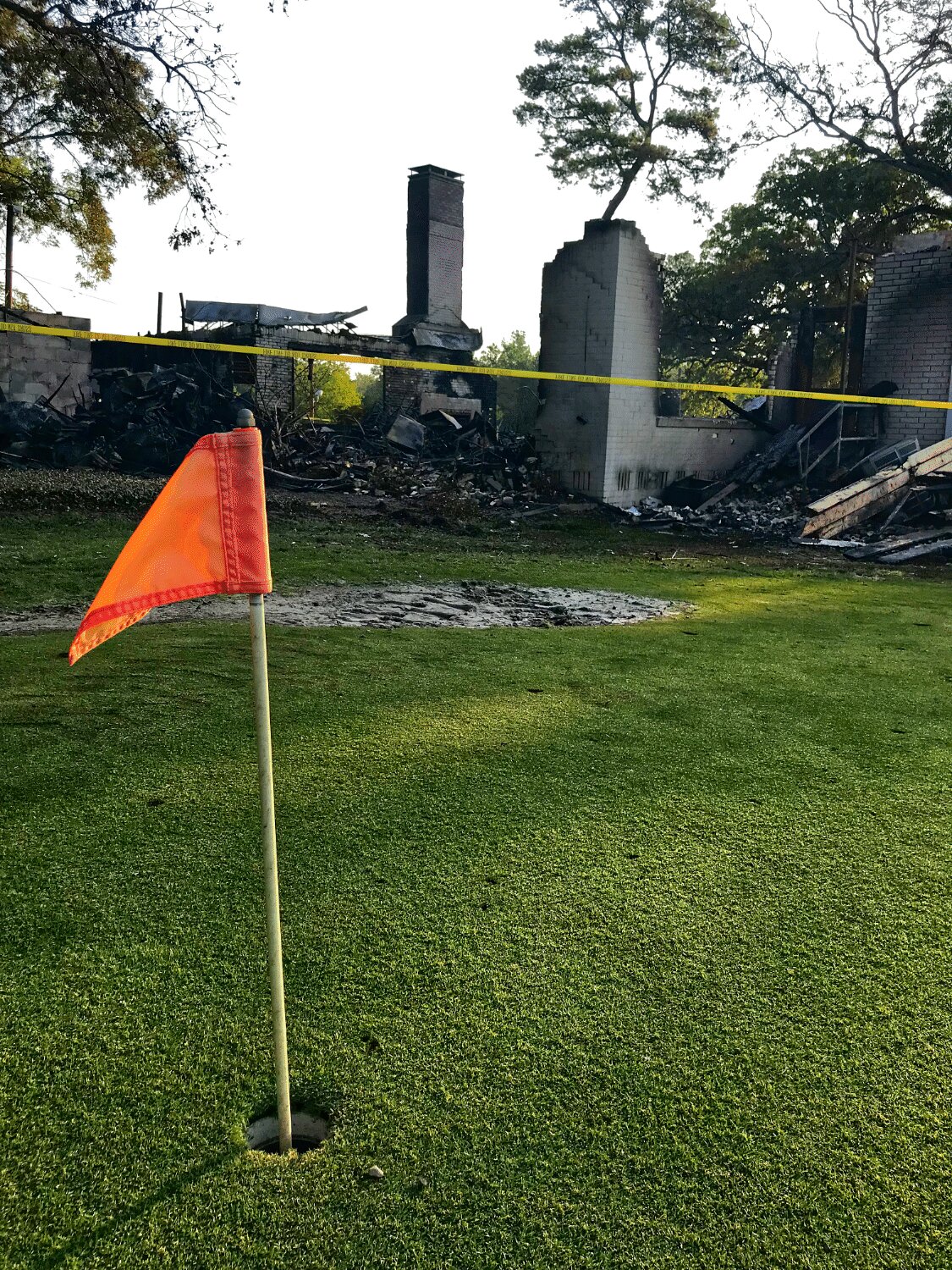 A flag holds firm on the putting green adjacent to the clubhouse, destroyed by fire mere hours earlier.